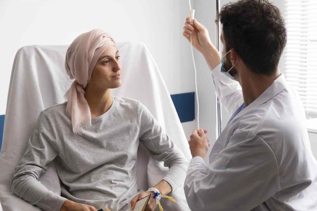 A paciente com câncer sentada em uma cadeira no hospital com um médico do lado ao se consultar sobre a síndrome mão-pé
