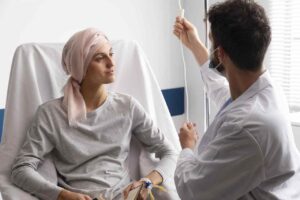 A paciente com câncer sentada em uma cadeira no hospital com um médico do lado ao se consultar sobre a síndrome mão-pé