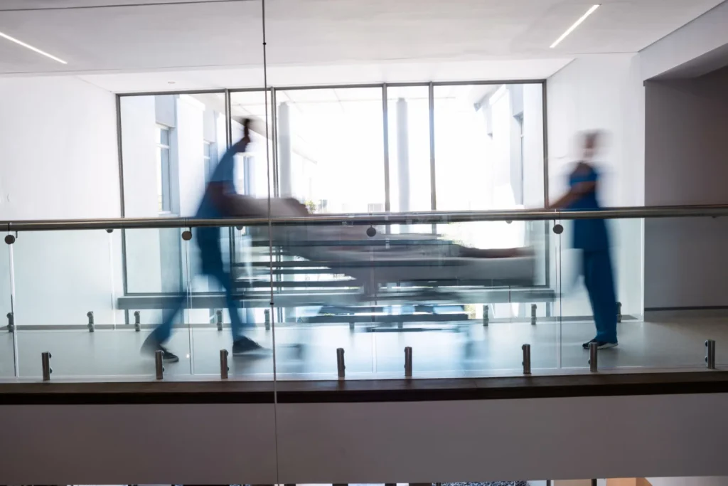 Profissionais de saude empurrando maca com paciente em corredor de hospital, representando urgencia no monitoramento de lactato