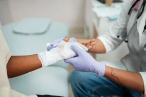 Profissional de saude com luvas realizando curativo na mao de paciente para tratamento de biofilme na ferida em consultorio