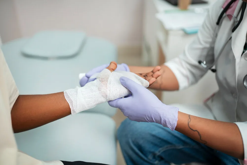 Profissional de saude com luvas realizando curativo na mao de paciente para tratamento de biofilme na ferida em consultorio