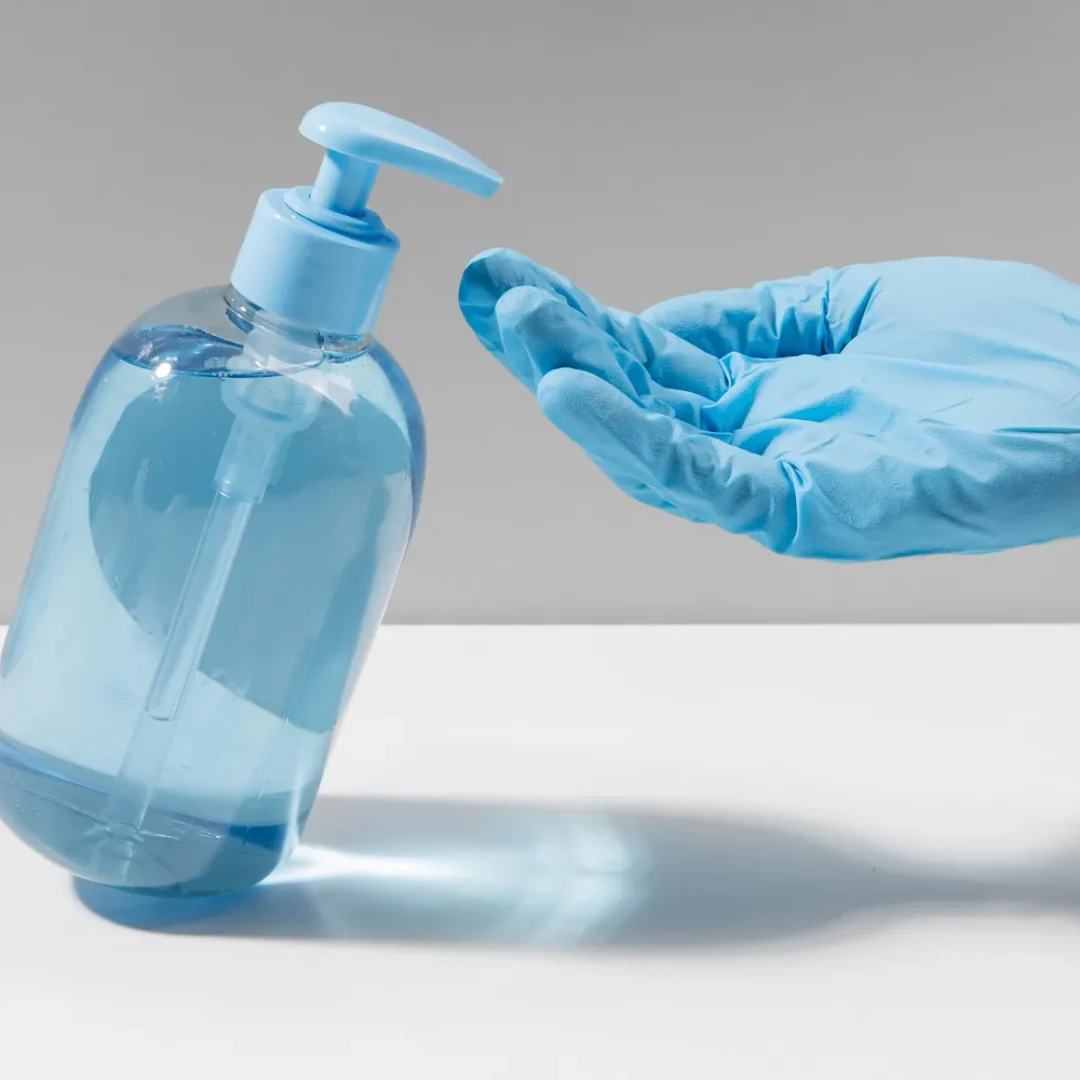 Mao com luva cirurgica azul recebendo gel alcoolico de frasco pump para antissepsia cirurgica das maos em ambiente hospitalar