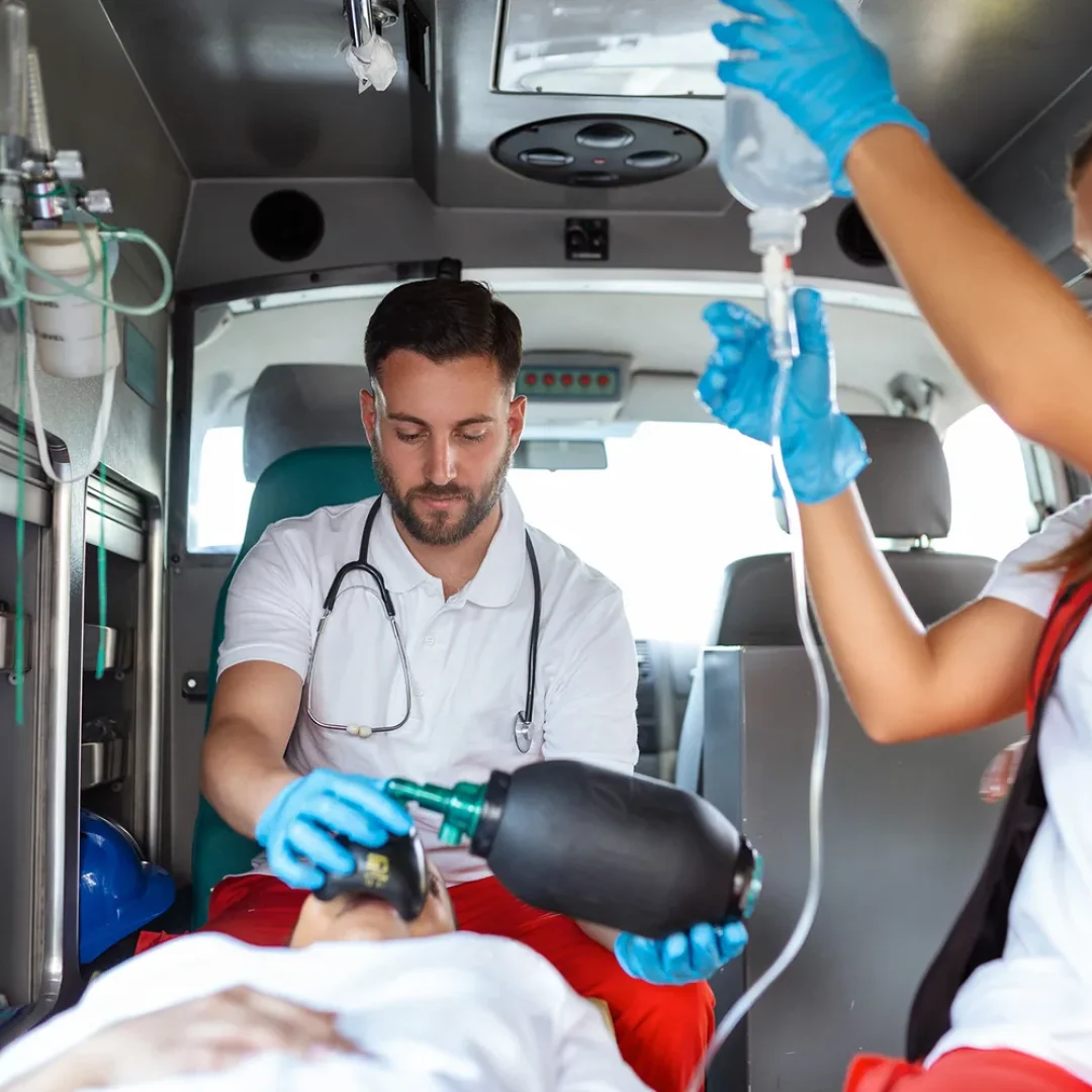 Dois socorristas realizando atendimento pre-hospitalar dentro de ambulancia com oxigenio e soro para paciente em maca
