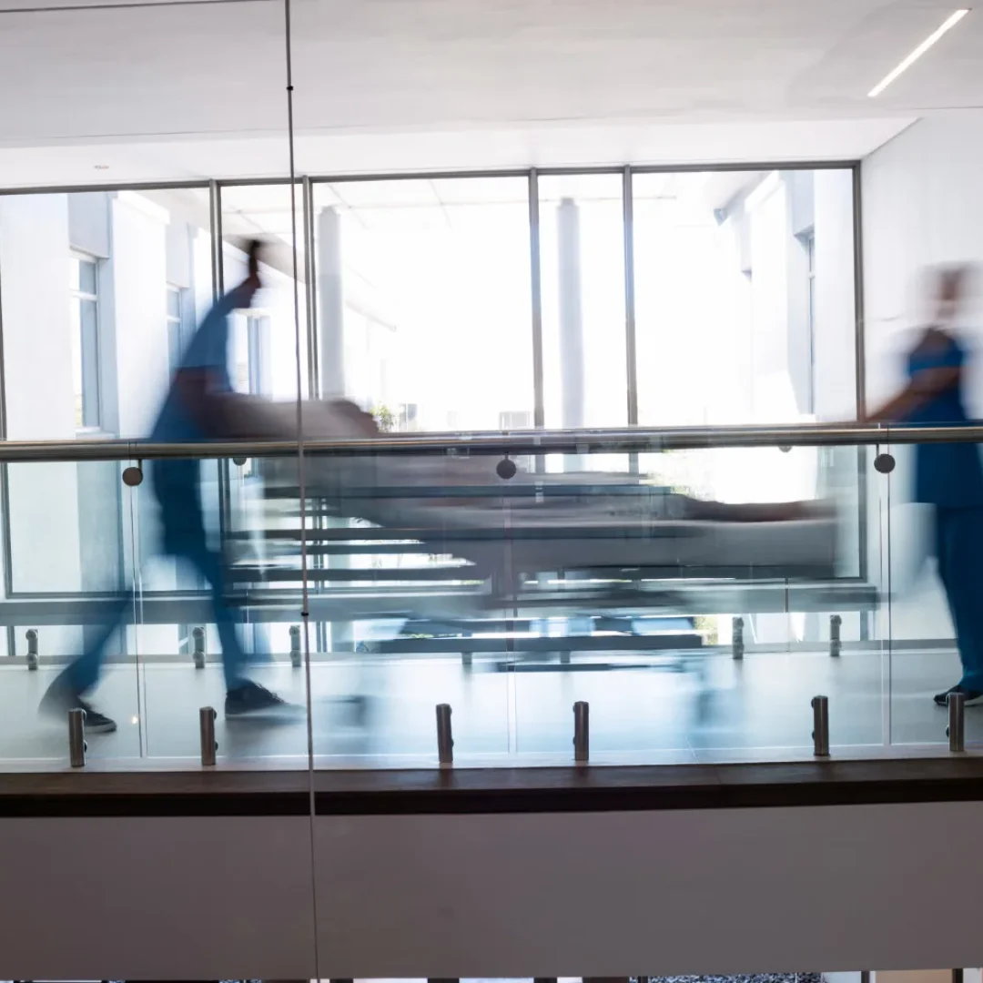Profissionais de saude empurrando maca com paciente em corredor de hospital, representando urgencia no monitoramento de lactato