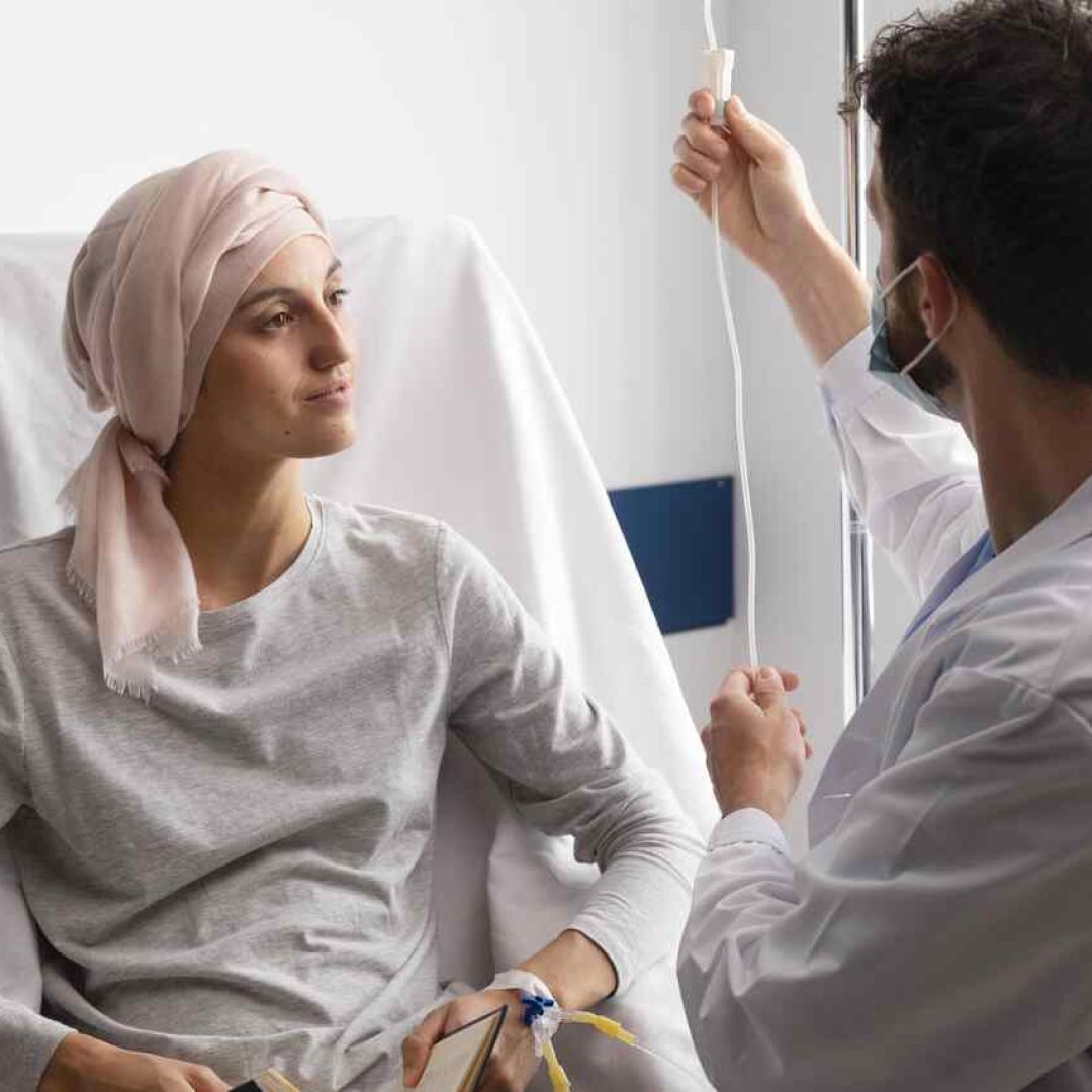 A paciente com câncer sentada em uma cadeira no hospital com um médico do lado ao se consultar sobre a síndrome mão-pé